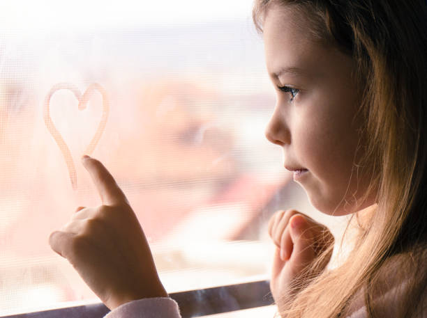 Little girl draws a heart on the window