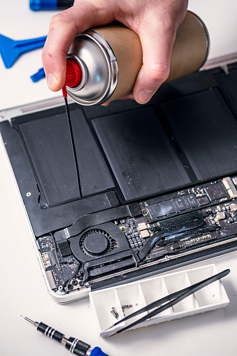 Close-up of a technician fixing a modern laptop computer. Ideal for illustrating the “right to repair” movement. Colour, horizontal format with some copy space.