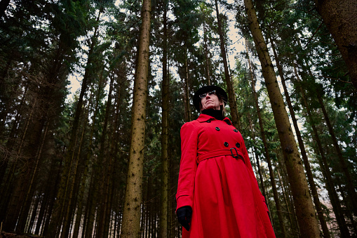 Outdoors portrait of woman in red. Standing in forest wearing hat - low angle view