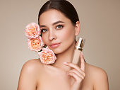 Beautiful young woman with foundation bottle and rose flowers