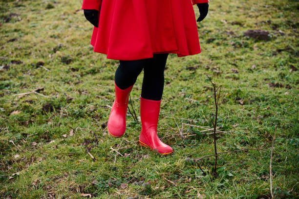 Outdoors portrait of woman in red. Rear view of walking white woman with long hair wearing warm clothing. Walking in meadow with red rubber boots