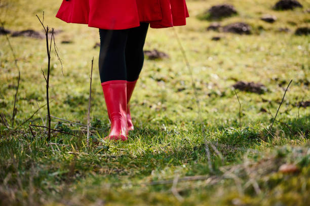 Outdoors portrait of woman in red. Rear view of walking white woman with long hair wearing warm clothing. Walking in meadow with red rubber boots