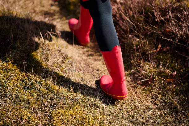 Outdoors portrait of woman in red. Rear view of walking white woman with long hair wearing warm clothing. Walking in meadow with red rubber boots