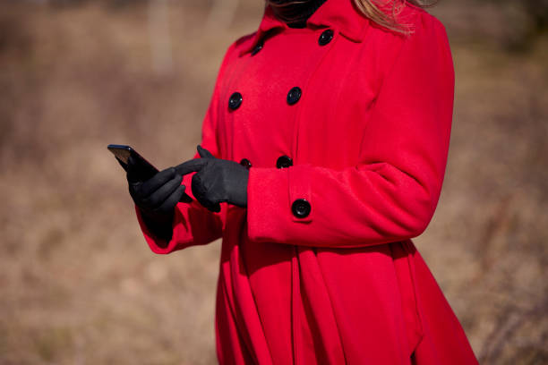 Outdoors portrait of woman in red. Part of. Woman in red coat holding mobile device in her hands with black gloves