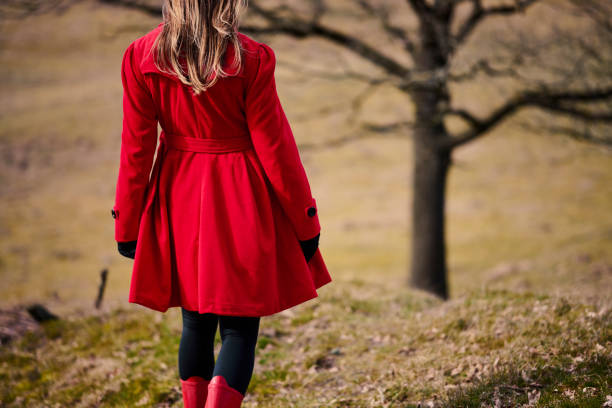 Outdoors portrait of woman in red. Rear view of walking white woman with long hair wearing warm clothing. Walking in meadow with red rubber boots