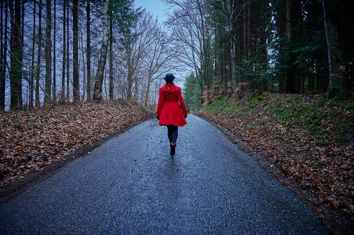 Outdoors portrait of woman in red. Walking on single lane road in forest