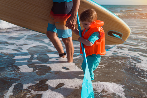 Man and his son getting into the sea with a paddleboard.