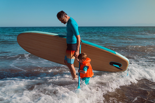 Man and his son getting into the sea with a paddleboard.