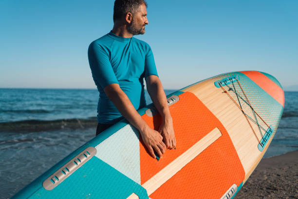 istock Man on the beach holding a paddleboard 1475276684