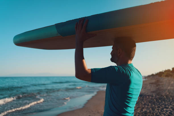 istock Man carrying paddleboard on his head and getting into the sea 1475276770