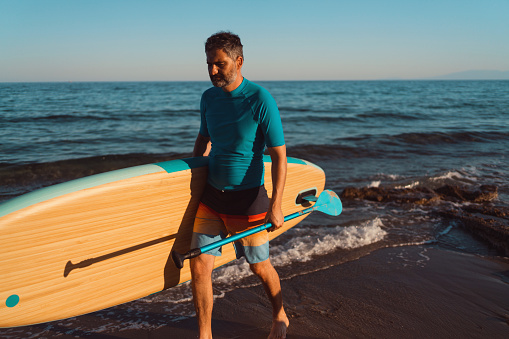 Man walking out of the sea with a paddleboard.