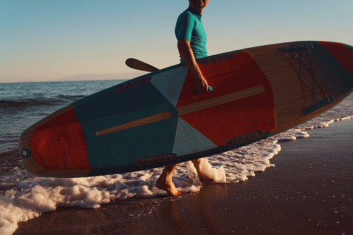 Man walking out of the sea with a paddleboard.