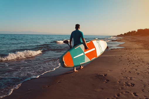 Man walking on the beach with a paddleboard.