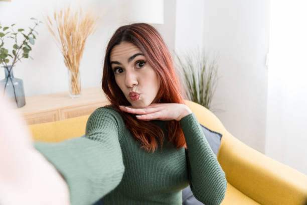istock Smiling woman sitting on sofa and looking at camera taking a selfie 1475279292