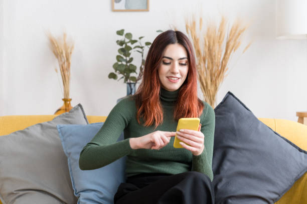 istock Young woman with smartphone sitting on sofa 1475280560