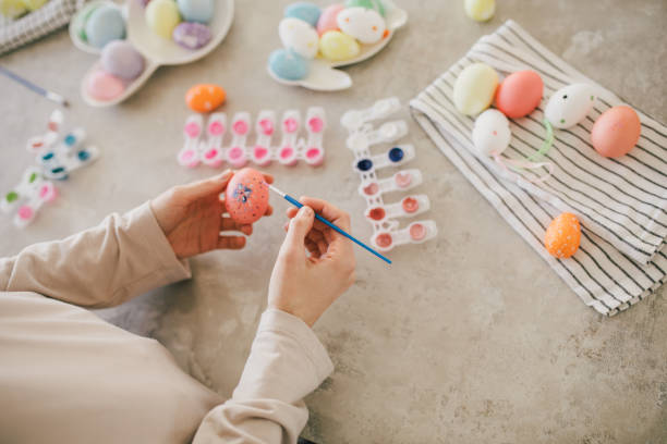 istock Young woman decorating Easter eggs using brush and paint on the kitchen. 1475281039