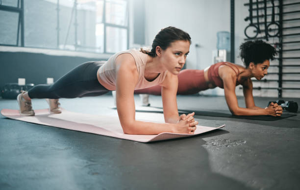 donna, fitness e corpo intero in plank per l'allenamento di base, l'esercizio fisico o l'allenamento insieme in palestra. donne che fanno esercizi addominali intensi in equilibrio sul tappetino per una parte superiore del torace forte e sana in palestra - torsolo di mela foto e immagini stock