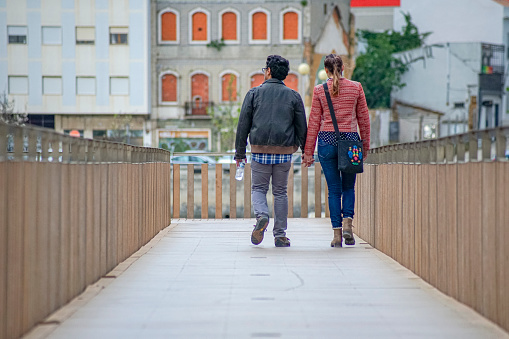 Pedestrian bridge over the Tagus river from the footbridges of Alburrica do Moinho Grande with two people walking hand in hand as a couple and residential buildings in the background, city of Barreiro