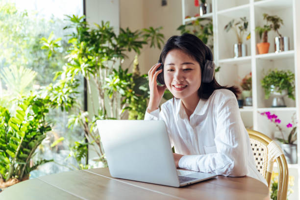 fêmea asiática em fones de ouvido usando laptop para comunicação on-line e bate-papo por vídeo - sitting area - fotografias e filmes do acervo