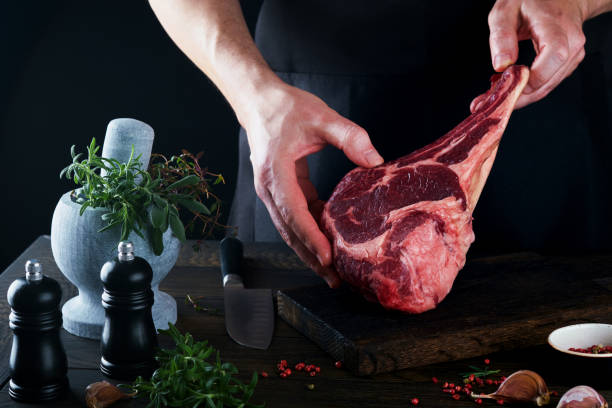 istock Chef cutting steak beef. Mans hands hold raw steak Tomahawk on rustic wooden cutting board on black background. Cooking, recipes and eating concept. Selective focus. 1475287588