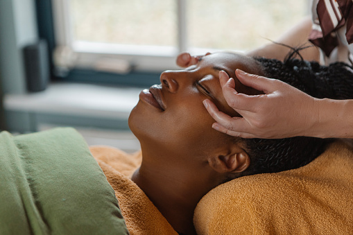 Professional salon facial massage treatment for a relaxed beautiful black woman during a pampering moment