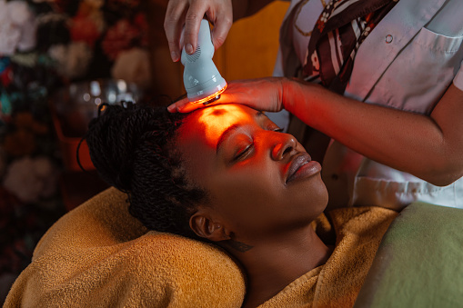 Professional salon colour therapy facial massage treatment for a relaxed beautiful black woman during a pampering moment