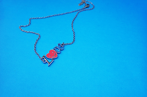 A creative top down view of image of the word love in the form of a luminous silver chain necklace, isolated on a blue background
