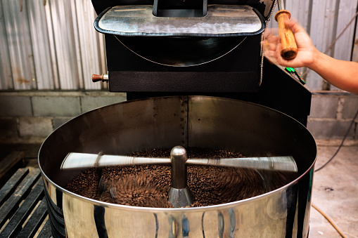 Coffee roaster machine at coffee roasting mixing process. Roasted spinning cooler professional machines and fresh brown coffee beans at factory, low speed shutter movement and motion blur coffee grain, concept