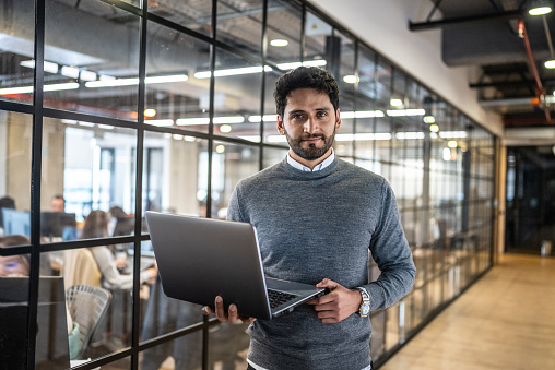 Portrait of a mid adult businessman holding laptop in the corridor at office