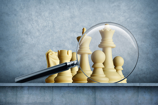 A magnifying glass rests in front of several chess pieces.