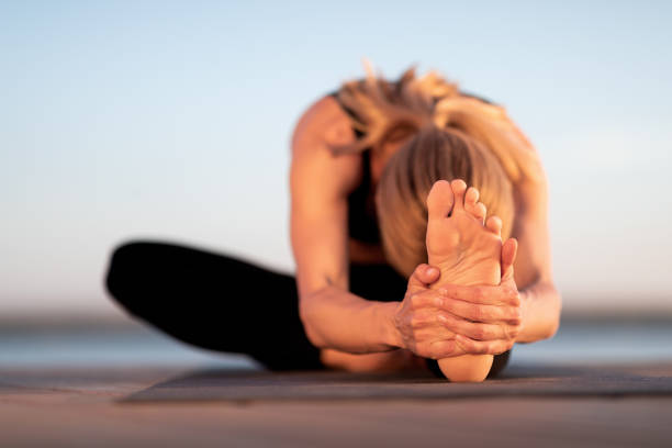 flexible junge frau, die sich dehnt, während sie yoga im freien praktiziert - nur frauen über 40 stock-fotos und bilder