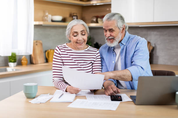 financial planning on retirement. senior couple with laptop and papers in kitchen - two parent family indoors home interior domestic kitchen imagens e fotografias de stock