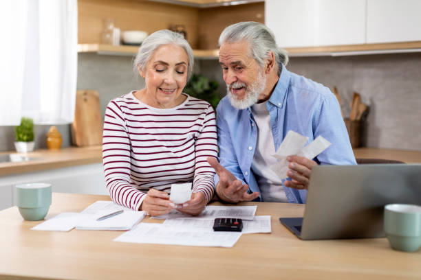 smiling elderly spouses checking receipts while planning family budget at home - two parent family indoors home interior domestic kitchen imagens e fotografias de stock