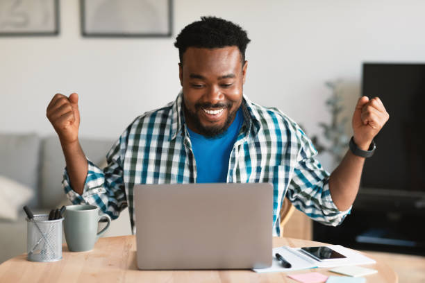 istock Joyful African American Guy Using Laptop Shaking Fists Sitting Indoors 1475307200