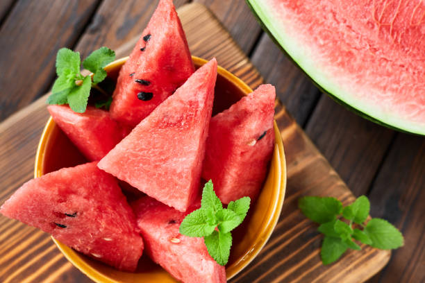 istock Sliced watermelon decorated with mint leaves on brown wooden background. Close-up, selective focus 1475309948