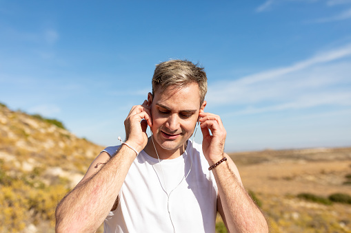 A man with gray hair listens to music with headphones during a walk in the countryside to lead a healthy lifestyle