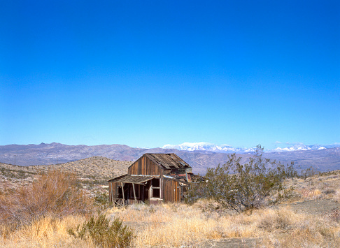 Abandoned ghost town house of wood in Californian desert with mountains at background