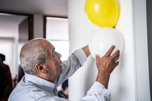 Senior man putting few balloons on the wall at home