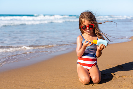 Little girl applying sunscreen lotion protection on the beach