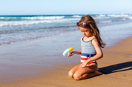 Little girl applying sunscreen lotion protection on the beach