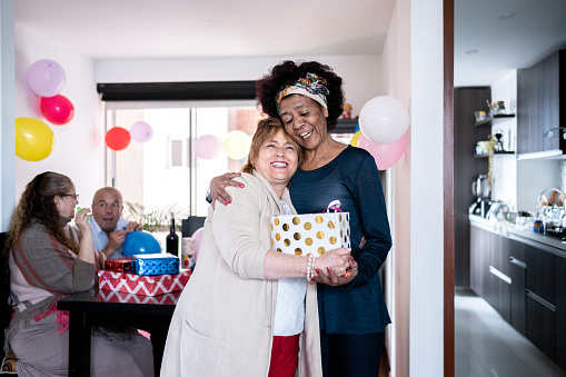 Senior woman embracing her friend after giving a birthday present at home