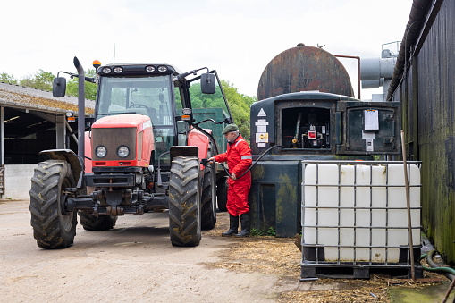 A shot of a male British farmer wearing red overalls and a flat refuelling an agricultural tractor on a sustainable farm in Northumberland in north east England.