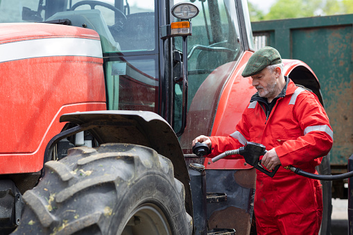 A shot of a male British farmer wearing red overalls and a flat refuelling an agricultural tractor on a sustainable farm in Northumberland in northeast England.
