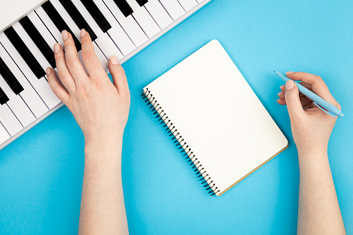 Female hands, blank notebook and music keys on blue background, flat lay, musical creativity concept.