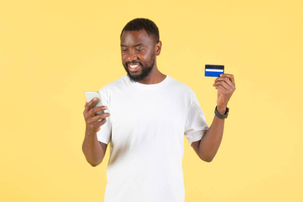 istock Black Guy Using Smartphone And Credit Card Shopping, Yellow Background 1475329074