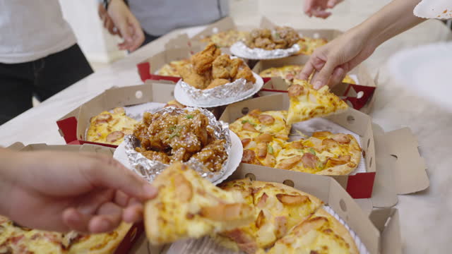 Hands picking up pieces of pizza and pieces of different fried chicken with sauce
