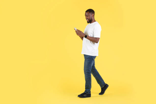 istock African American Guy Using Cellphone Texting Walking Over Yellow Background 1475329752