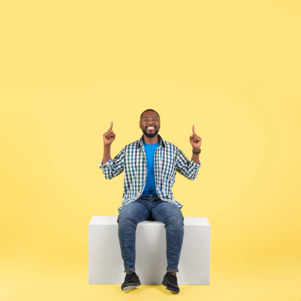 istock Black Guy Pointing Fingers Up Sitting Over Yellow Background, Square 1475341677