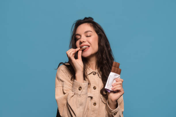 目を閉じた幸せなミレニアル世�代のヨーロッパ人女性は、チョコレートバーの味を楽しむ - copy space sweet food food chocolate ストックフォトと画像