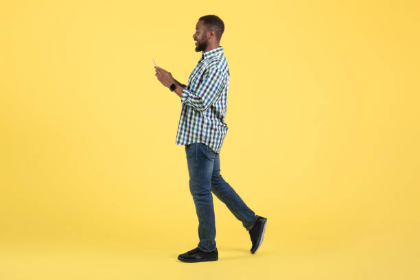 istock Happy African American Man Using Cellphone Walking Over Yellow Background 1475341881